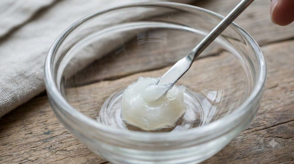 A close-up of a small glass bowl with Vaseline being mixed with a tiny spoon illustrating the preparation step for one o