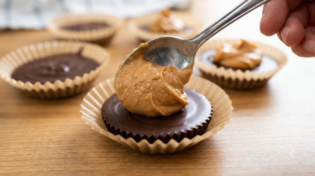 A close-up of the peanut butter filling being spooned onto the hardened chocolate base in a mini muffin liner showing th