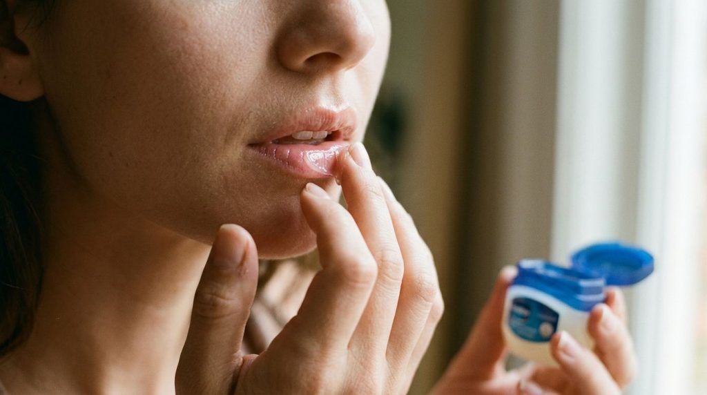 Close-up shot of a woman applying Vaseline to her lips creating a glossy moisturized look Her skin looks hydrated and he