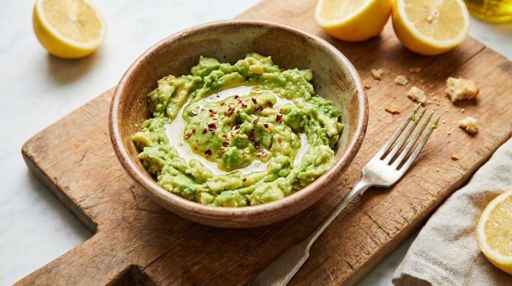 Mashed avocado with lemon juice in a bowl with a fork next to it
