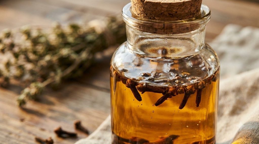 A close-up of a glass jar filled with a golden-hued oil and cloves representing the infused Botox Oil