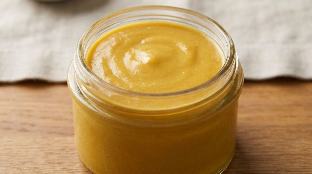 Close-up of a smooth golden-yellow Vaseline and turmeric mixture in a small glass jar ready for use