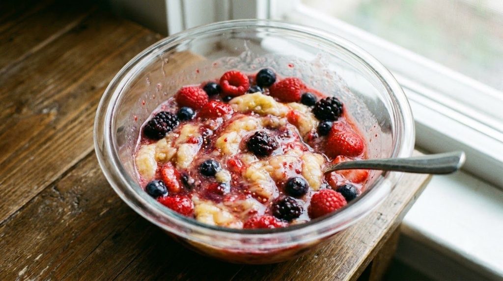 Mashed banana and mixed berries stirred together in a microwave-safe bowl before cooking