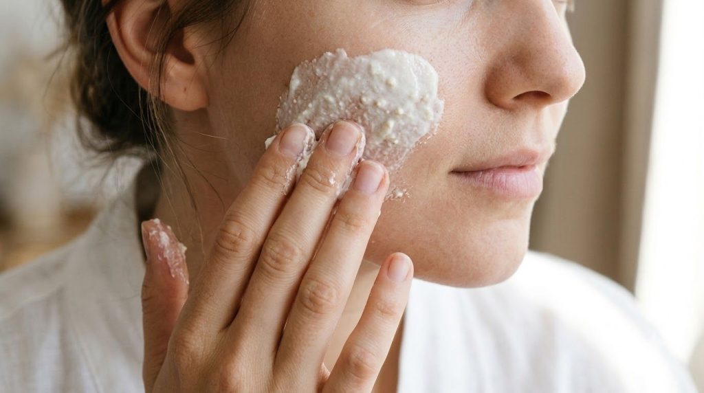 A woman s hand gently applying the homemade paste to her cheek showing the creamy texture of the mixture