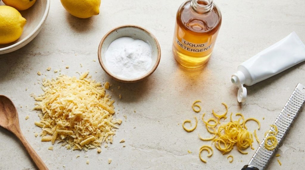 Various ingredients laid out on a clean kitchen counter a grated pile of soap a bowl of baking soda liquid detergent too
