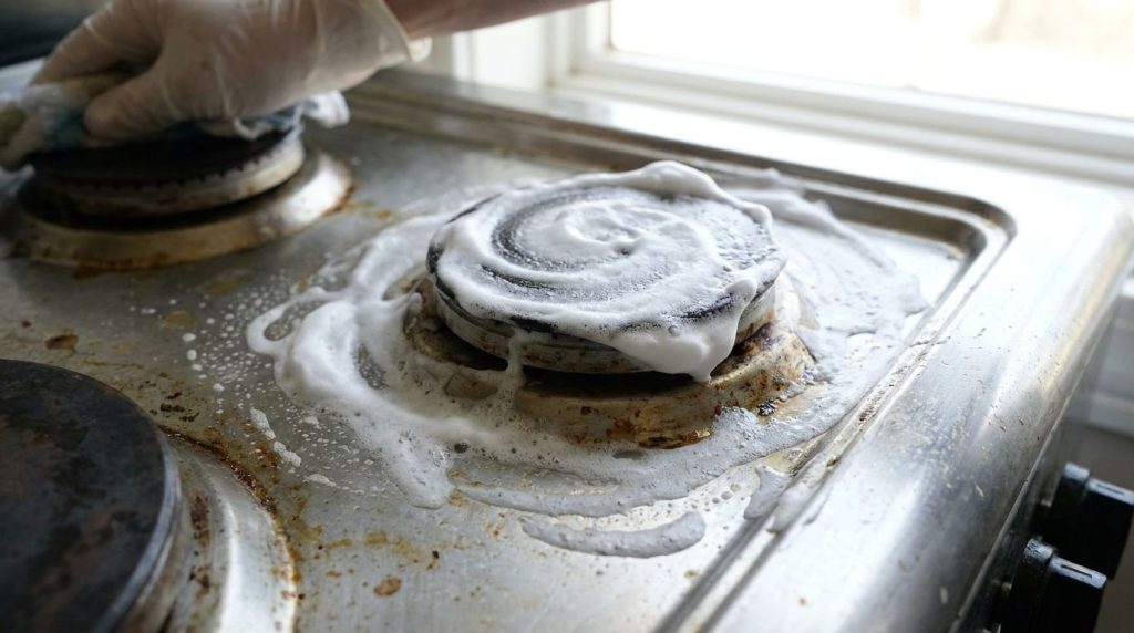 A greasy kitchen stove being cleaned with shaving cream showing the foam applied to the surface