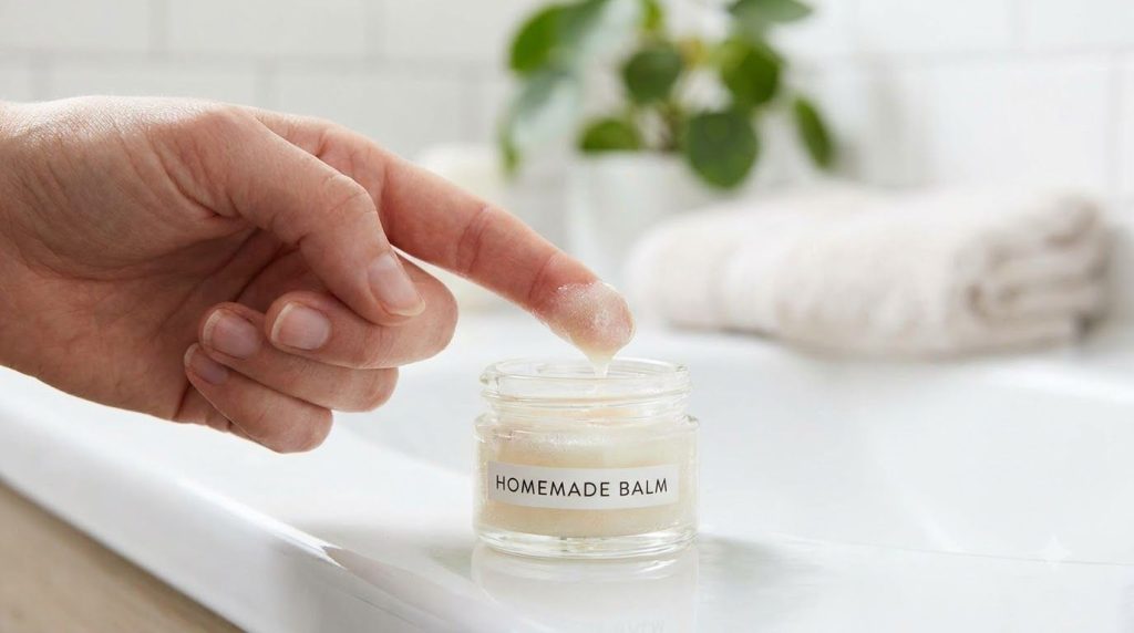 A small clear jar containing the mixed Vaseline and baby oil product with a finger scooping out a small amount in a soft