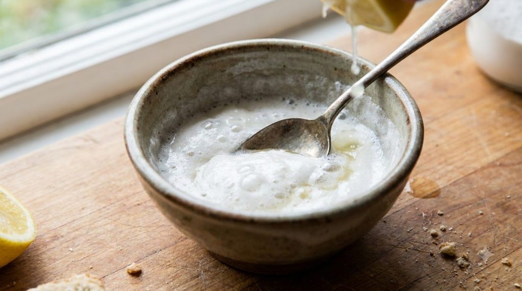 Close-up of a small bowl with baking soda white vinegar and lemon juice being mixed into a paste with a spoon