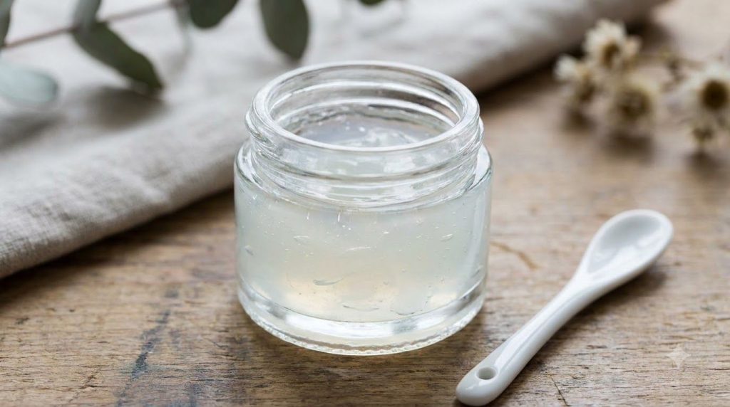 Close-up of a small glass jar containing the mixed Vaseline and Vitamin E glow gel with a small spatula beside it