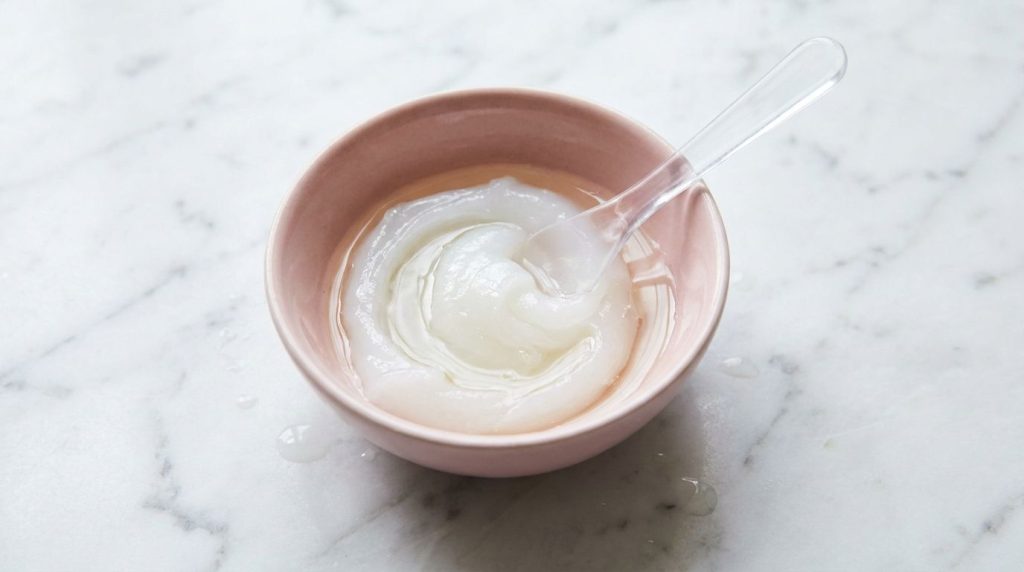 A small pink bowl containing Vaseline and baby oil being mixed with a small spatula