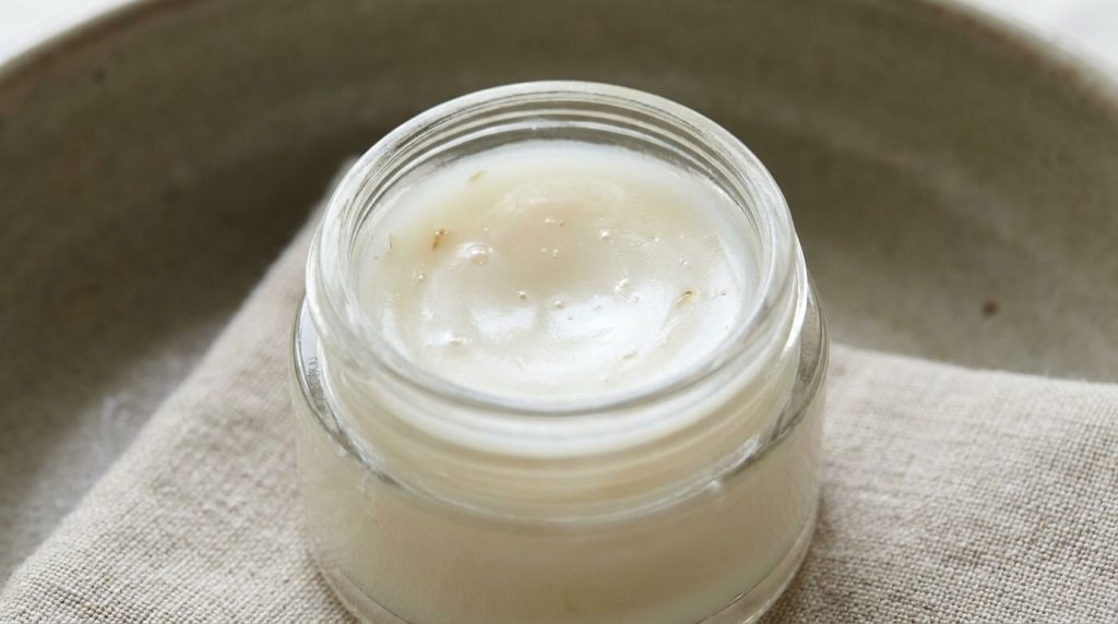 A close-up of the prepared DIY glass skin blend in a small clear jar with a smooth balm-like texture