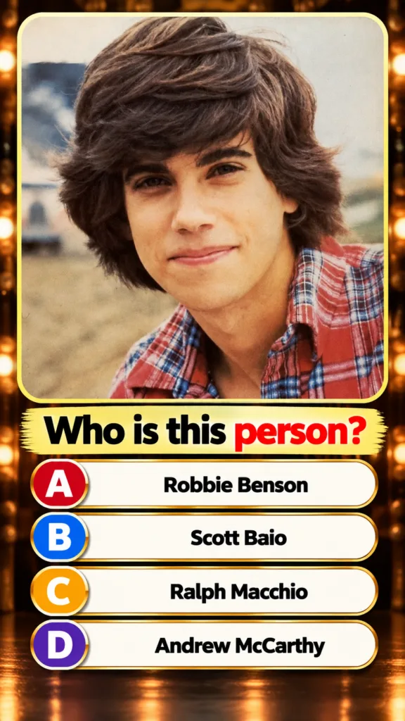 A classic headshot of a young Robbie Benson from the 1980s with shaggy brown hair and a plaid shirt smiling gently