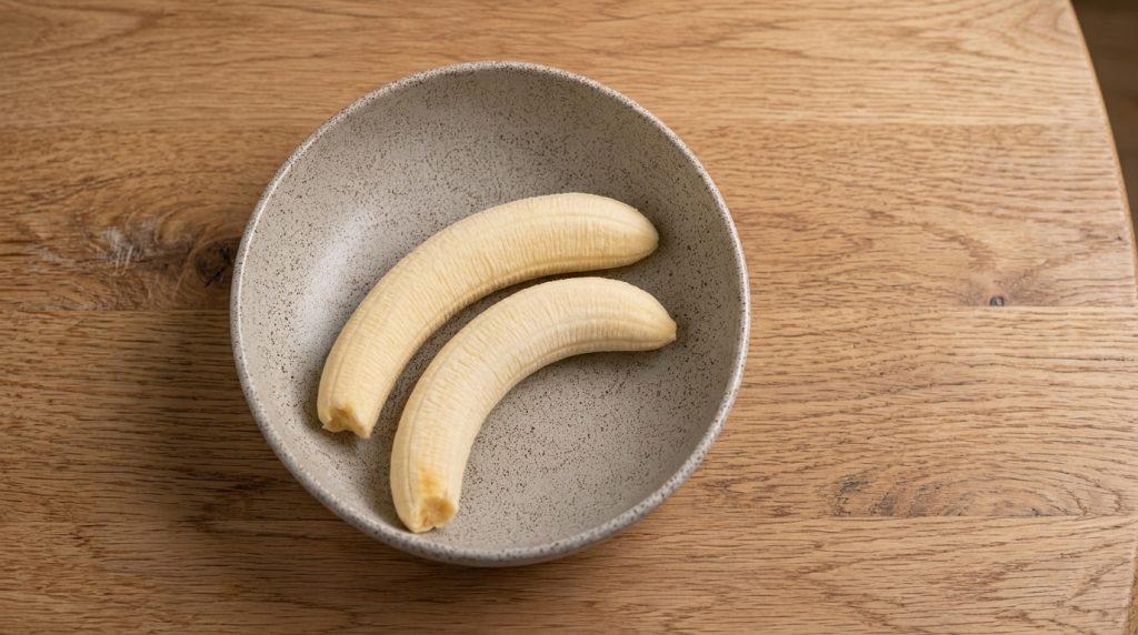 Two peeled ripe bananas in a light gray bowl on a wooden surface ready to be eaten as a healthy snack