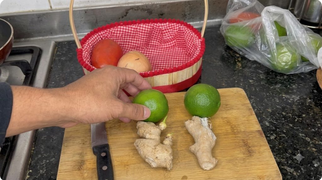 Overhead shot of fresh limes and ginger on a wooden cutting board with a hand reaching for a lime