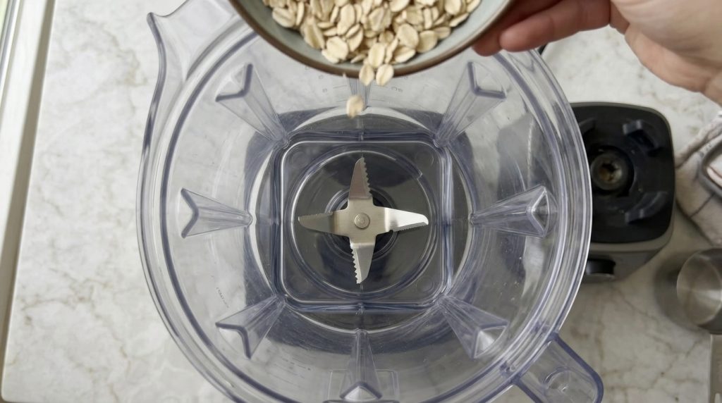 Blender jar with metallic blades and dry rolled oats about to be blended